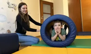 Chłopiec w okularach w tunelu terapeutycznym, obok uśmiechnięta terapeutka.