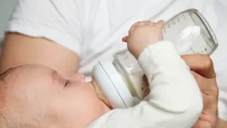 Dziecko pije mleko modyfikowane z butelki. Rodzic karmi malucha, dbając o jego potrzeby.