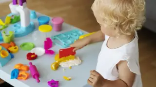 Mała blondynka bawi się masą plastyczną, rozwijając sensorykę. Kolorowe foremki i wałek czekają na kreatywne pomysły.