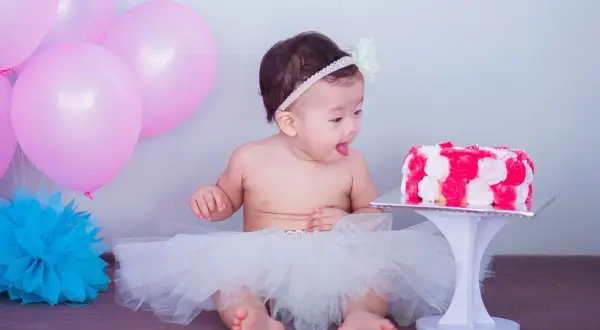 Słodki roczek! Dziecko w tiulowej spódniczce z zaciekawieniem patrzy na tort. Różowe balony dodają uroku.
