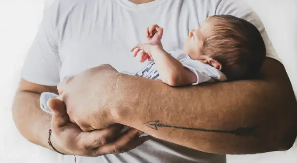 Ojciec trzyma dziecko, które wydaje się być w niewygodnej pozycji. Złe noszenie niemowlaka może być niebezpieczne.