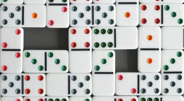 Wiele białych kostek do gry w domino z kolorowymi kropkami (zielonymi, czerwonymi, szarymi i pomarańczowymi) ułożonych w rzędy.