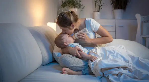 Matka karmi dziecko butelką w łóżku, czule całując je w czoło. Nawet koszmary senne nie są straszne, gdy czuwa kochająca mama.