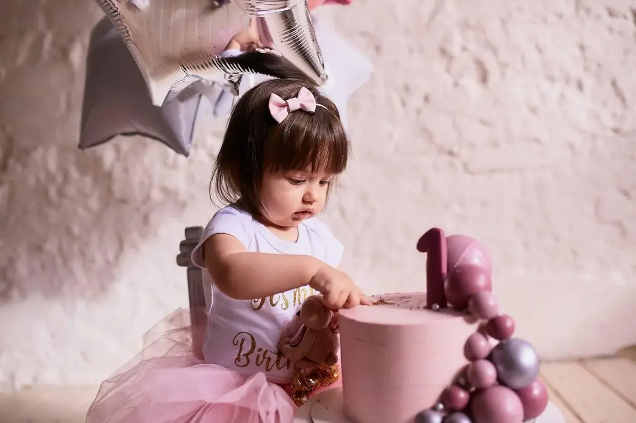 Urocza dziewczynka w różowej tiulowej spódniczce i body z napisem "Birthday" przy pierwszym torcie. Idealny pomysł, co dla dziecka na roczek!