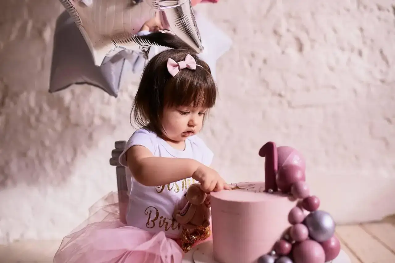 Urocza dziewczynka w różowej tiulowej spódniczce i body z napisem "Birthday" przy pierwszym torcie. Idealny pomysł, co dla dziecka na roczek!