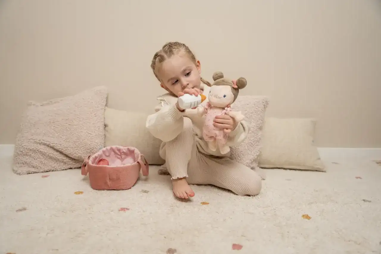 Dziewczynka karmi butelką swoją ulubioną marionetkę, która wygląda jak małe dziecko.