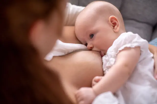 Malutkie dziecko z niebieskimi oczami karmione piersią. Trudno określić, ile mleka wypija noworodek, ale ten maluch wygląda na zadowolonego.