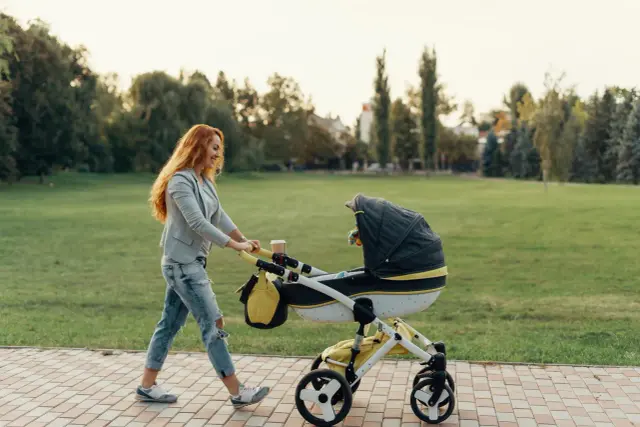 Radosny pierwszy spacer z noworodkiem w wózku po parku.